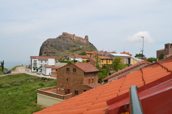 Vista de un castillo sobre una colina y casas de colores en un paisaje montañoso.