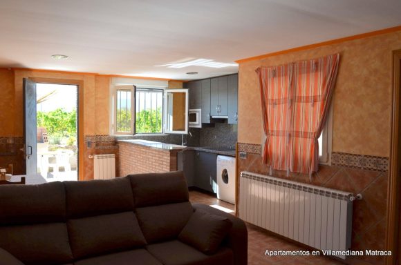 Interior de un apartamento con cocina, salón y ventanales iluminados.