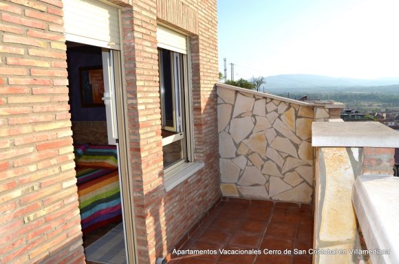 Balcón de un apartamento con vista al paisaje montañoso y una cama de colores en el interior.